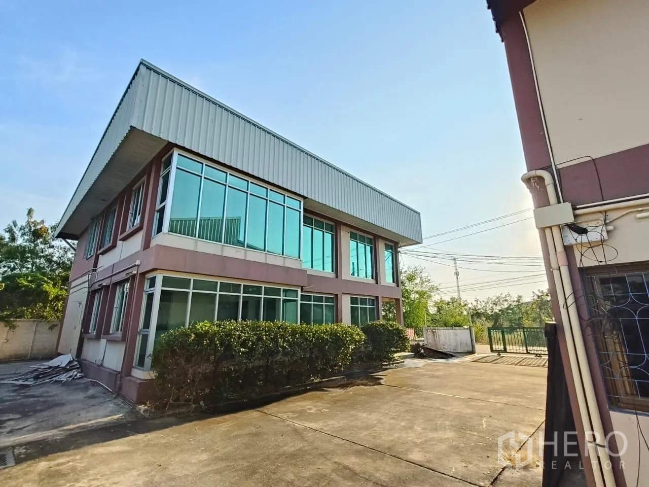 คลังสินค้า ให้เช่าหรือขายในMin Buri, Bangkok - อาคารออฟฟิศกระจกมุมเชื่อมต่อโกดัง หน้าต่างบานใหญ่ ลานคอนกรีตกว้าง และประตูรั้วสีเขียว