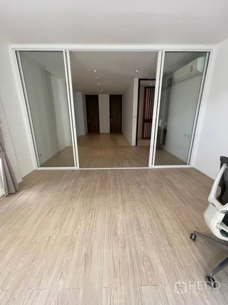 Home Office for rent in Khlong Toei, Bangkok - Spacious workspace facing sliding glass doors with wood-look floors, white walls, split air conditioning and an office chair.