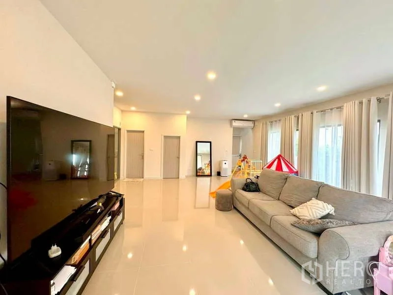 独立式住宅 出售在Lat Krabang, Bangkok - 大客厅，长沙发、电视墙、通透窗与筒灯。