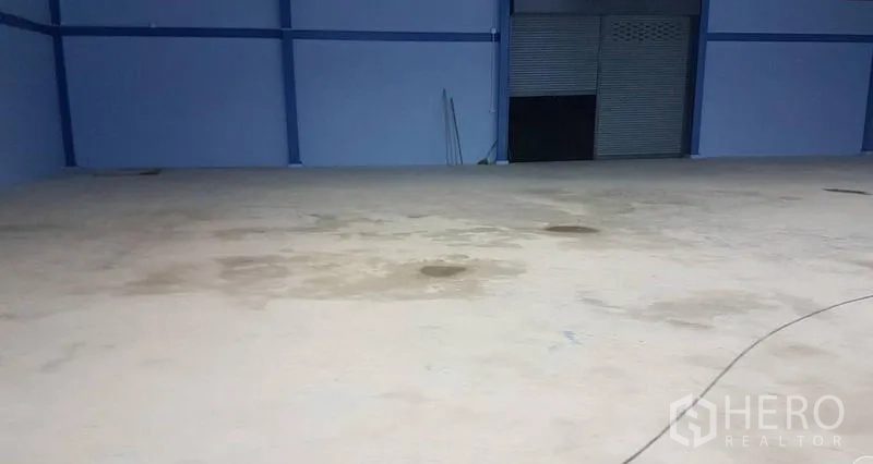 Warehouse for sale in Mueang Nonthaburi, Nonthaburi - Empty warehouse floor facing a roller shutter door for loading.