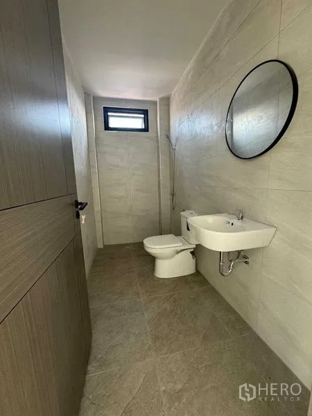 Home Office for rent in Don Mueang, Bangkok - Compact bathroom with wall-mounted sink, round mirror and toilet in a tiled finish.
