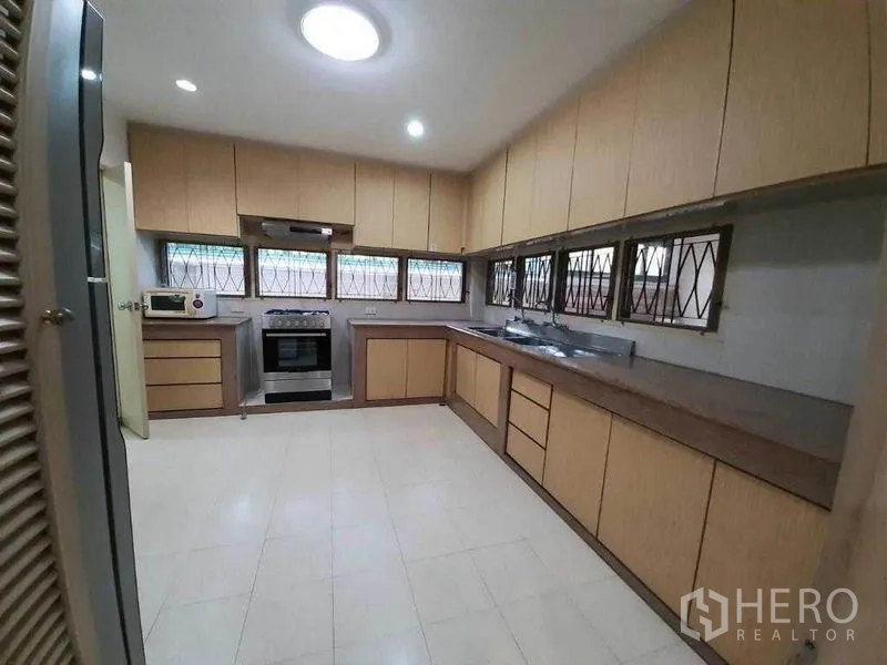 Detached House for rent in Watthana, Bangkok - Large kitchen with long countertops, ample wood cabinetry, windows, oven and range hood.