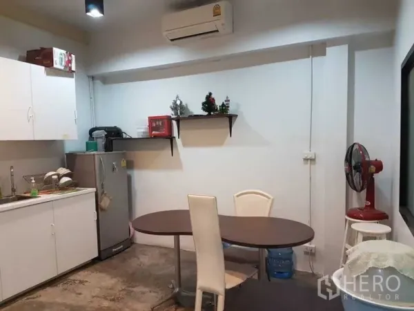 Shophouse for sale in Bang Rak, Bangkok - Compact pantry with white cabinets, refrigerator and oval dining table in a simple workspace.