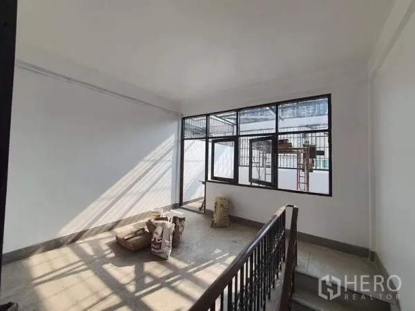 Shophouse for rent in Bangkok - Upper-floor landing with metal stair railing and wide grilled windows letting in strong natural light.