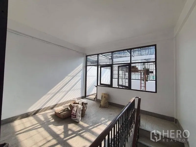 Shophouse for rent in Bangkok - Upper-floor landing with metal stair railing and wide grilled windows letting in strong natural light.