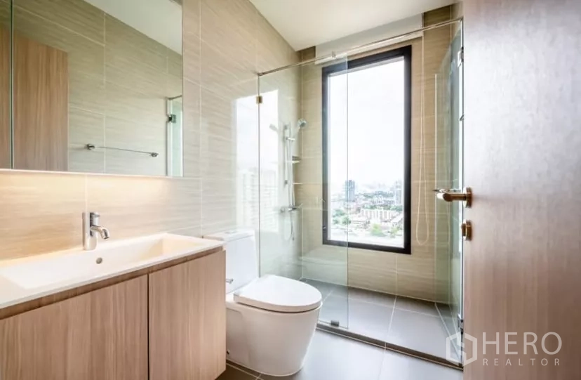 Condominium for rent in Chatuchak, Bangkok - Modern bathroom with glass shower enclosure and window overlooking the city.