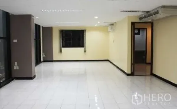 Office Space for rent in Bang Rak, Bangkok - Spacious open-plan office with glossy white tiles, ceiling lights, wide windows and a doorway to an internal room.