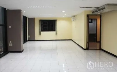 Office Space for rent in Bang Rak, Bangkok - Spacious open-plan office with glossy white tiles, ceiling lights, wide windows and a doorway to an internal room.