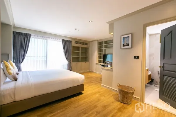Apartment for rent in Watthana, Bangkok - Primary bedroom with large window, built-in shelving and workspace, with ensuite bathroom entrance.
