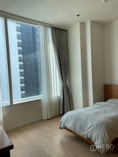 公寓 出租在Watthana, Bangkok - 明亮次卧，转角大窗、浅色木地板与灰色窗帘。