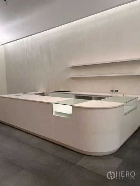 Standalone for rent in Khlong Toei, Bangkok - U-shaped white sales or reception counter with shelving and concealed lighting.