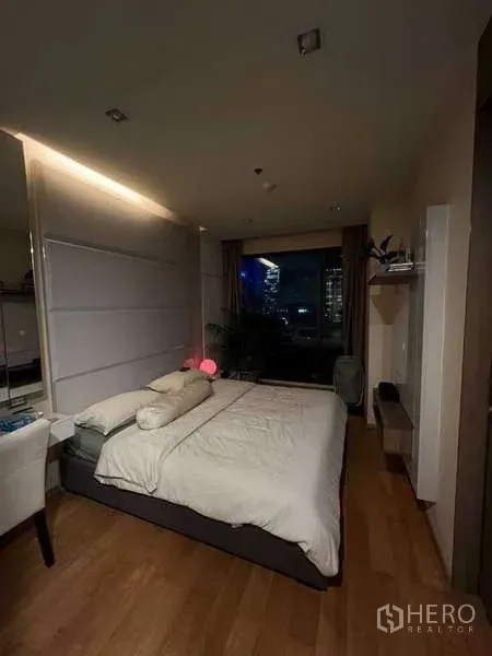 Condominium for rent in Bang Rak, Bangkok - Cozy bedroom with city night view through a floor-to-ceiling window.