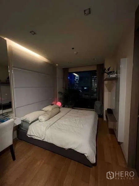 Condominium for rent in Bang Rak, Bangkok - Cozy bedroom with city night view through a floor-to-ceiling window.
