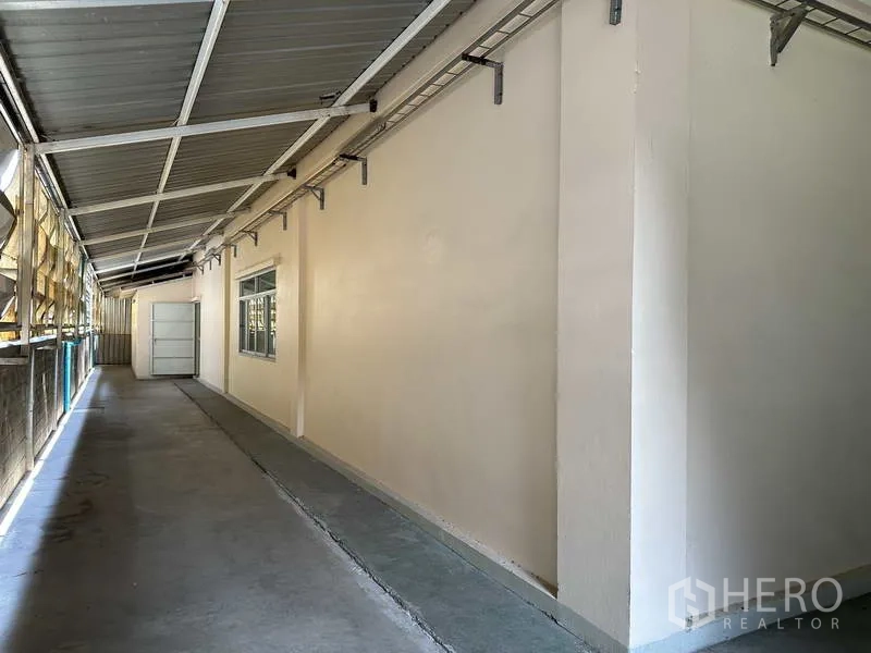 Factory for rent in Samut Prakan - Covered service corridor beside the factory with metal roof and cable trays.
