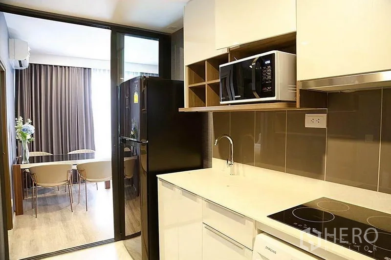 公寓 出租在Huai Khwang, Bangkok - 简洁厨房，白色台面，玻璃移门后为用餐区。