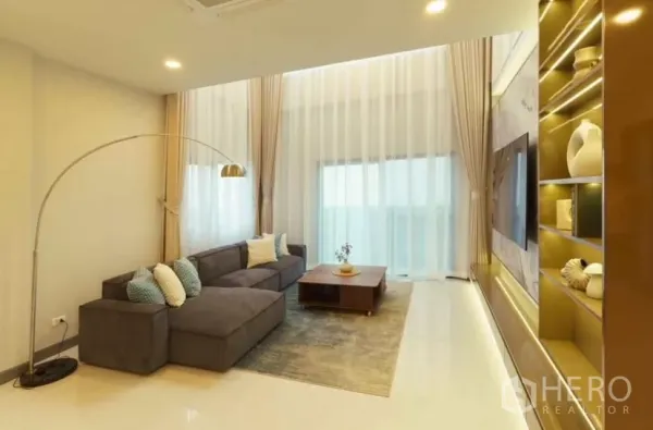 独立式住宅 出租或出售在Bang Phli, Samut Prakan - 明亮客厅，L形沙发、通高纱帘与电视墙。