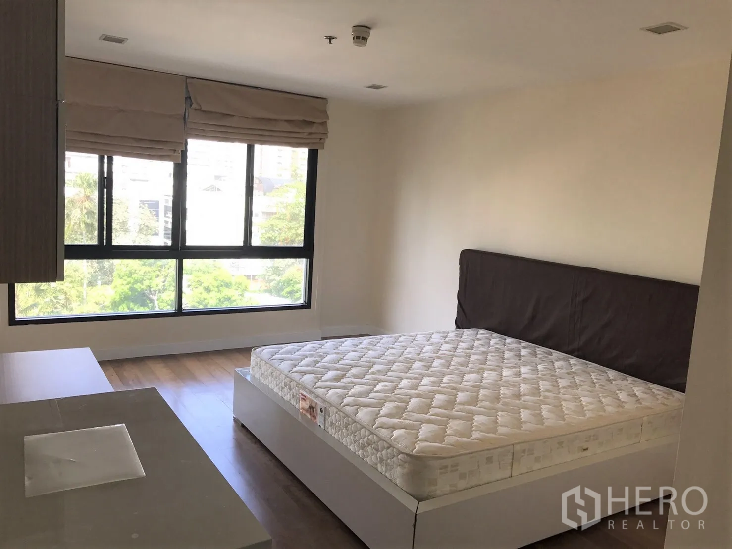 公寓 出租或出售在Watthana, Bangkok - 宽敞卧室，转角大窗配罗马帘，木地板上摆放床。