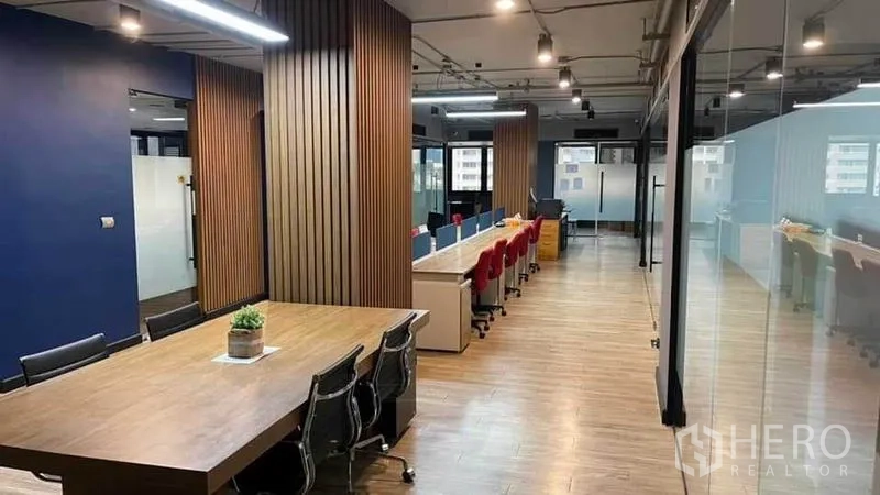 Office Space for rent in Khlong Toei, Bangkok - Open-plan office with long rows of workstations, glass meeting rooms and wood-slat columns.