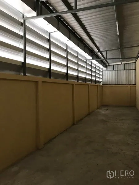 Warehouse for rent in Samut Sakhon - Interior aisle of the warehouse with high metal roof and louvered vents allowing natural light.