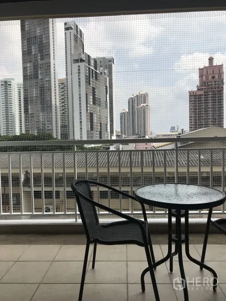 Condominium for rent in Khlong Toei, Bangkok - Covered balcony with bistro set overlooking the city skyline and high-rises.