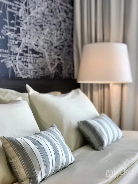 Condominium for rent in Khlong Toei, Bangkok - Close-up of neatly made bed with striped pillows and bedside lamp against map wallpaper.