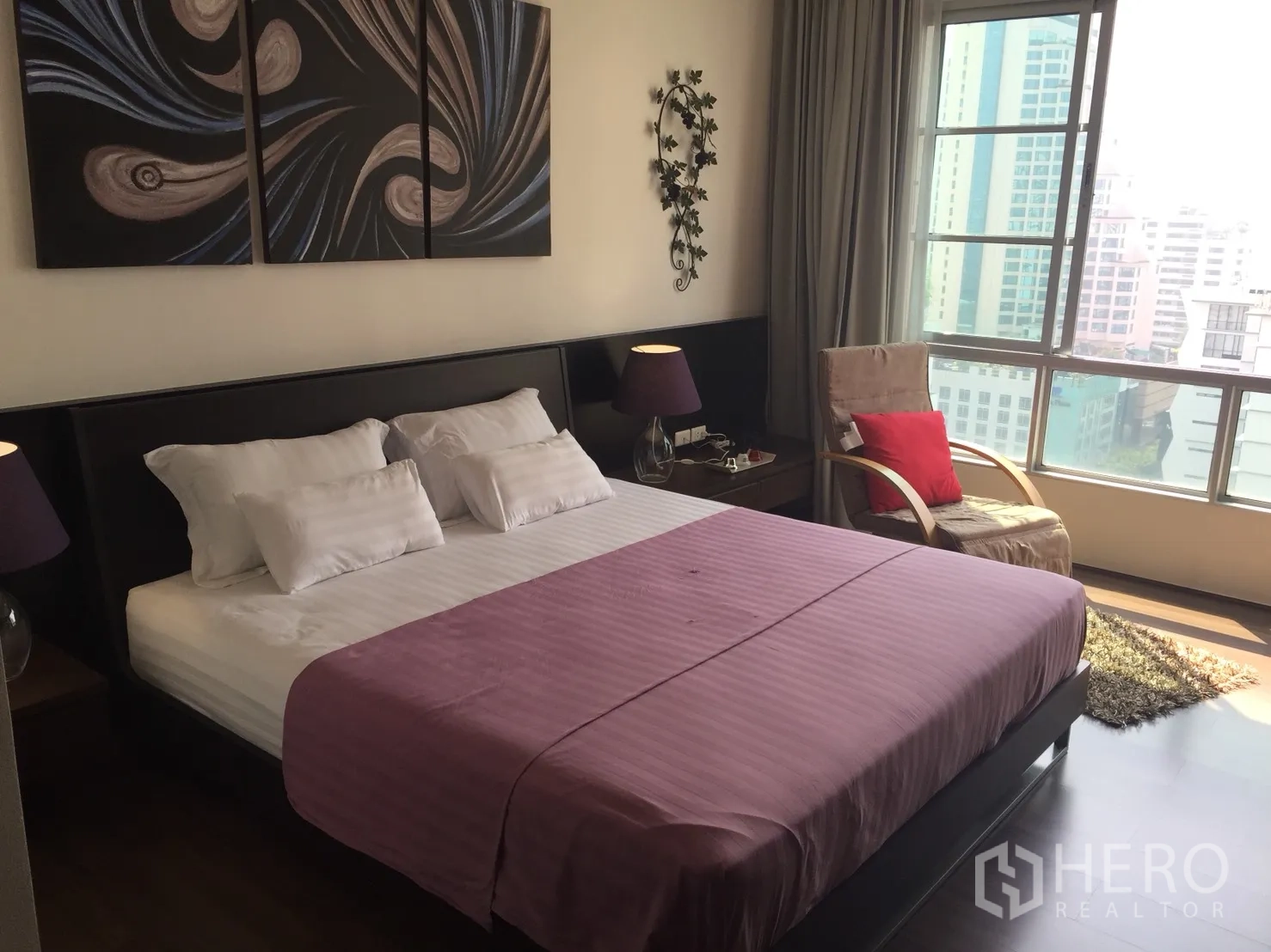 Condominium for rent in Khlong Toei, Bangkok - Master bedroom with king bed, bedside lamps, wall art, and large city-view window.