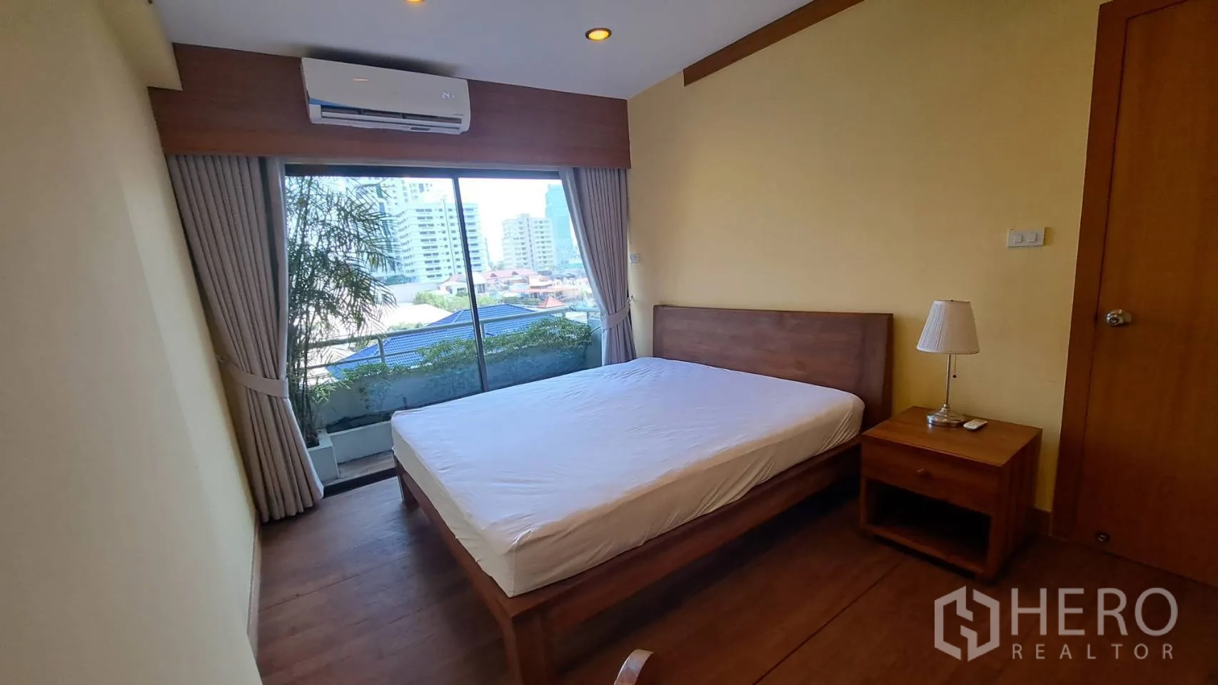 Condominium for rent in Khlong Toei, Bangkok - Bedroom with sliding glass doors opening to a leafy balcony.