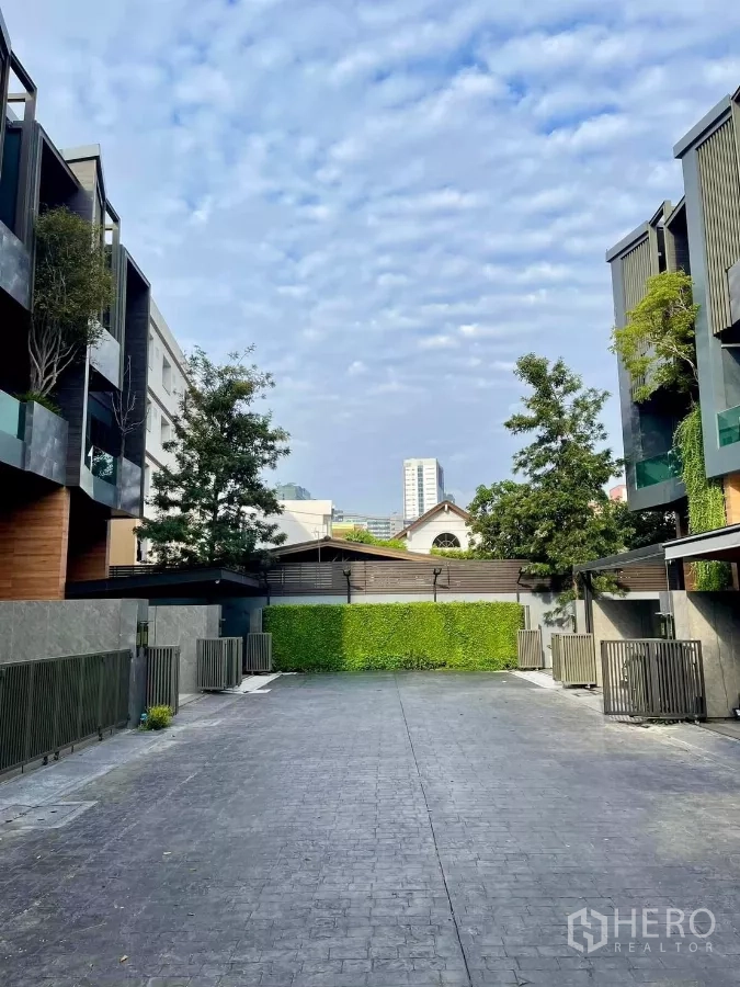 联排别墅 出租在Chatuchak, Bangkok - 社区私密车道，两侧现代黑木风联排与绿篱、晴朗天空。