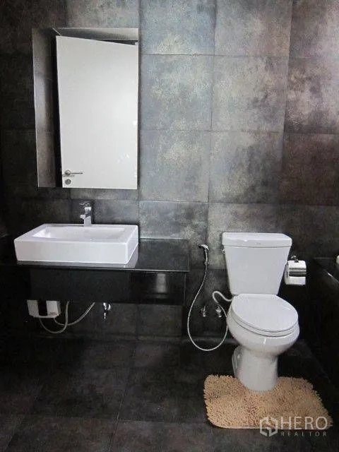 Condominium for rent in Khlong Toei, Bangkok - Modern bathroom with dark tiles, square basin, mirror, and toilet.
