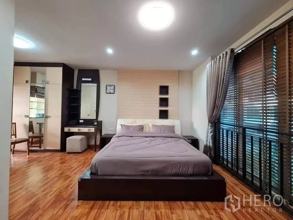 Townhouse for rent in Khlong Toei, Bangkok - Spacious master bedroom with wood flooring, large windows with blinds and curtains, dressing table and wardrobes.