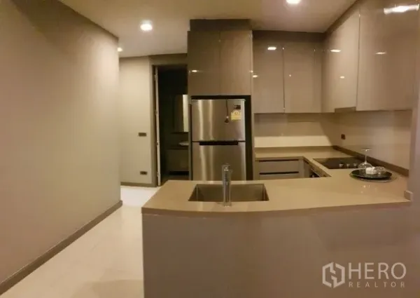 Condominium for rent in Bang Rak, Bangkok - Modern L-shaped kitchen with island, glossy cabinetry and a stainless steel fridge.
