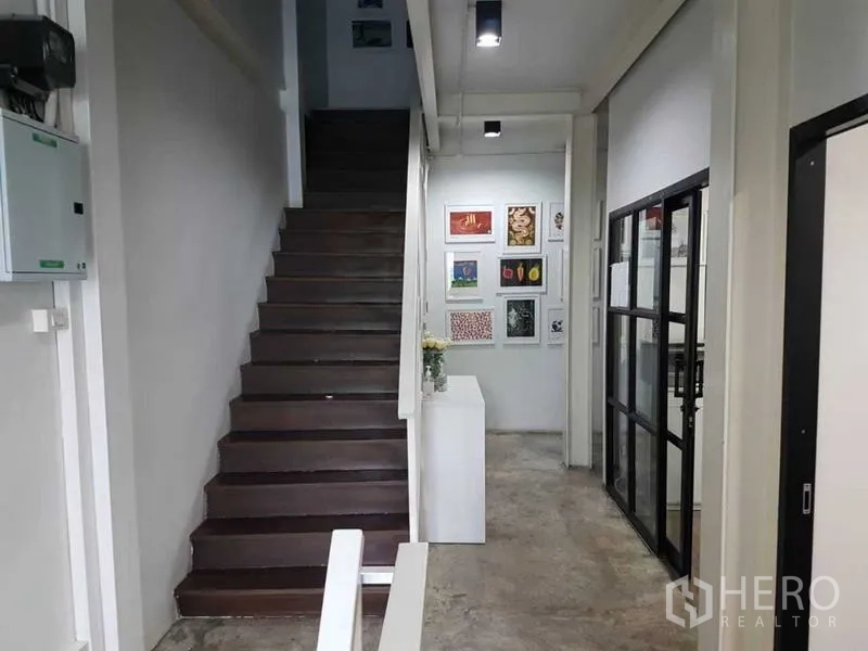 Shophouse for sale in Bang Rak, Bangkok - Interior hallway with wooden staircase, concrete floor and glass-partitioned office.