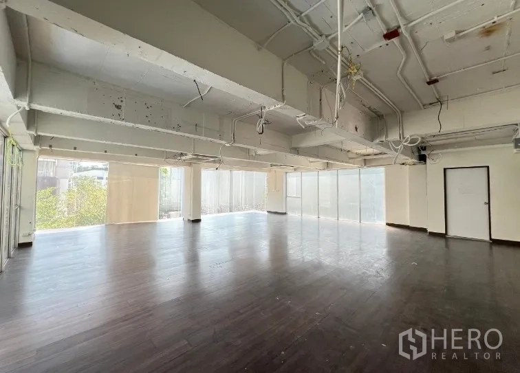 Retail Space for rent in Watthana, Bangkok - Large empty unit with industrial-style ceiling, support columns and frosted glass panels along two sides.