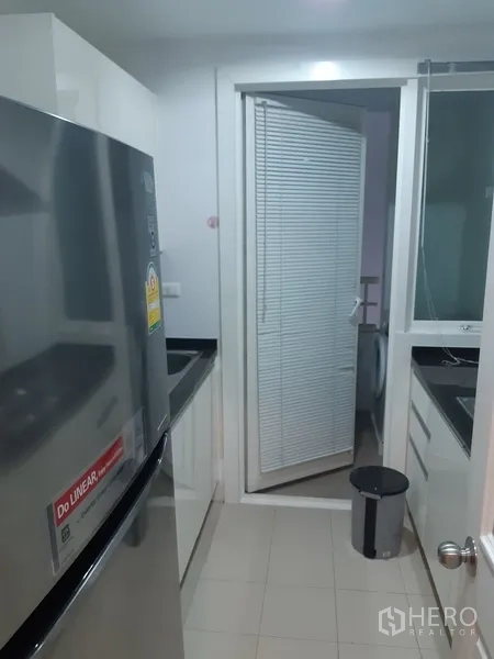 Condominium for rent in Khlong Toei, Bangkok - Separate galley kitchen with refrigerator, black countertops and utility area with washing machine.