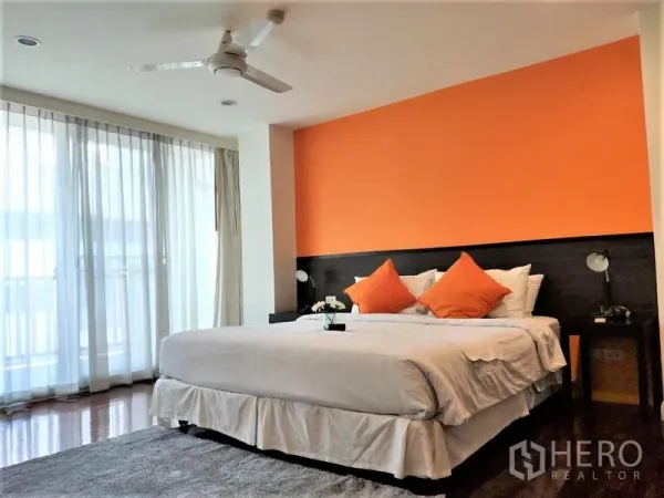 公寓 出租在Bang Rak, Bangkok - 次卧配橙色特色墙，大床、吊扇和通往阳台的落地窗。