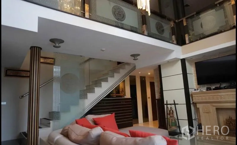 公寓 出租在Khlong Toei, Bangkok - 客厅配玻璃栏杆楼梯、装饰壁炉和上方夹层。