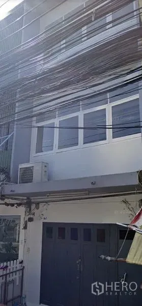 Shophouse for rent in Watthana, Bangkok - Three-storey shophouse exterior with wide front doors, windows and an air-conditioning unit.