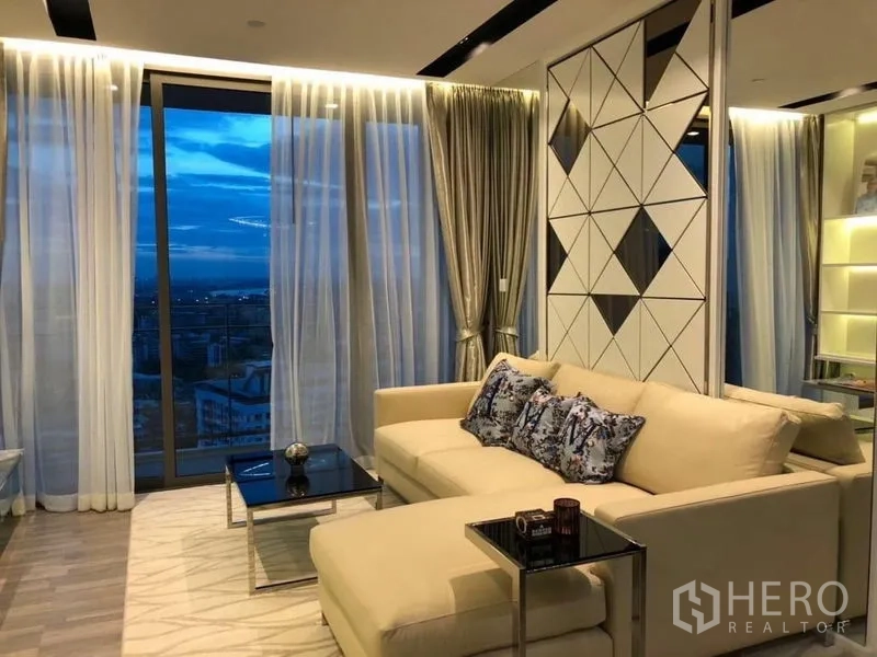 Condominium for rent or sale in Watthana, Bangkok - Contemporary living room with cream sofa, floor-to-ceiling windows and city sunset view.
