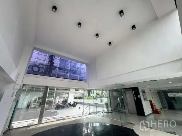 零售空间 出租在Bang Rak, Bangkok - 挑高零售内部，筒灯照明，玻璃入口，街景可见。