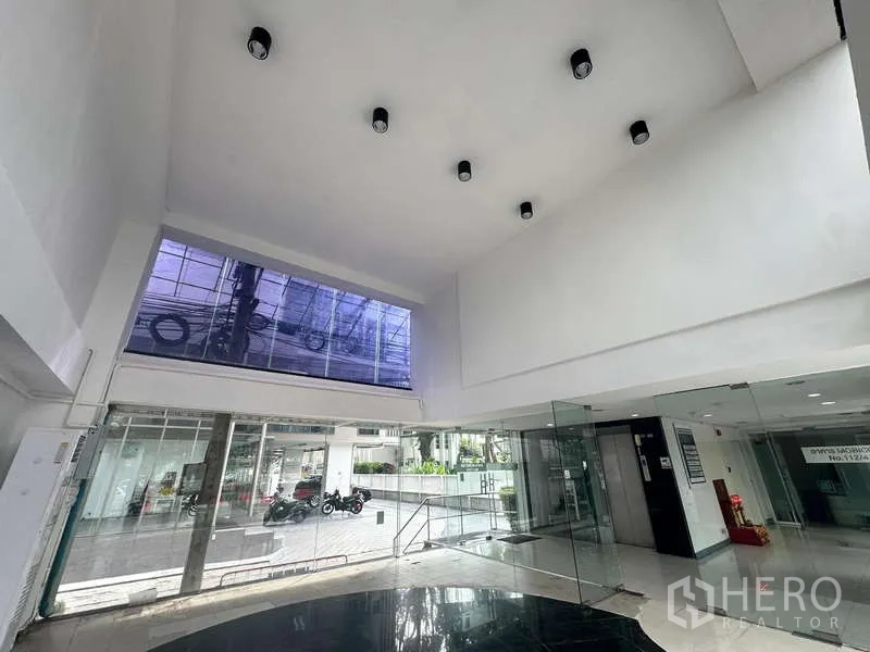 零售空间 出租在Bang Rak, Bangkok - 挑高零售内部，筒灯照明，玻璃入口，街景可见。