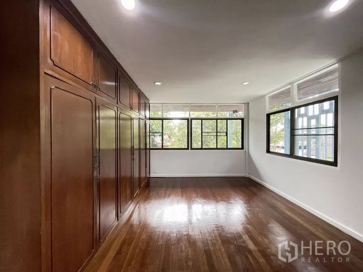 Home Office for rent in Din Daeng, Bangkok - Bedroom featuring a full wall of wooden built‑in wardrobes and corner windows.