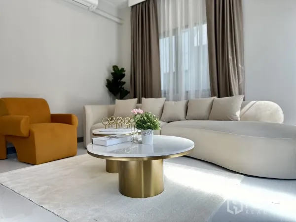 Detached House for rent or sale - Bright living room with curved cream sofa, mustard armchair, gold marble-topped coffee tables and sheer curtains.