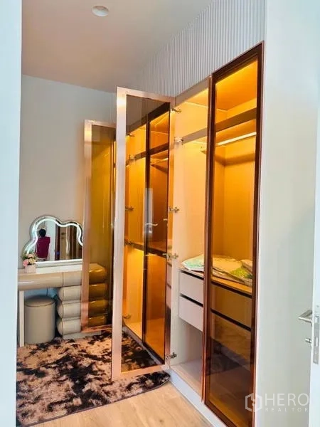 Detached House for rent or sale in Bang Kapi, Bangkok - Walk‑in closet with amber glass wardrobes, built‑in drawers and a vanity with stool.