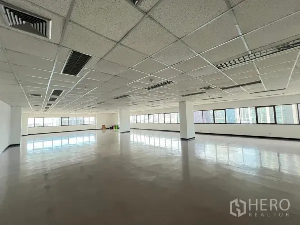 สำนักงาน ให้เช่าหรือขาย - พื้นที่สำนักงานแบบเปิดกว้าง ฝ้าเพดานทีบาร์ ไฟฟลูออเรสเซนต์ และหน้าต่างยาวมองวิวสกายไลน์กรุงเทพฯ