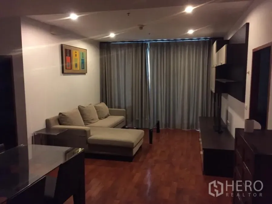公寓 出租或出售在Khlong Toei, Bangkok - 客厅温馨，L 形沙发、木地板、电视墙与全遮光窗帘。
