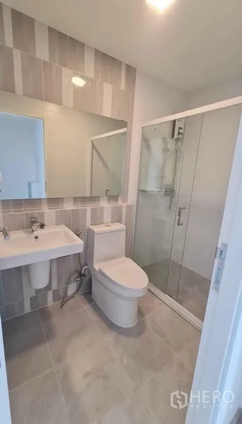 Townhouse for rent in Prawet, Bangkok - Second bathroom featuring striped wall tiles, large mirror and shower enclosure.