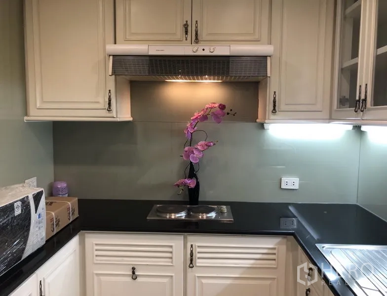 Condominium for rent or sale in Sathon, Bangkok - Kitchen counter with range hood, black granite worktop and orchid decoration.