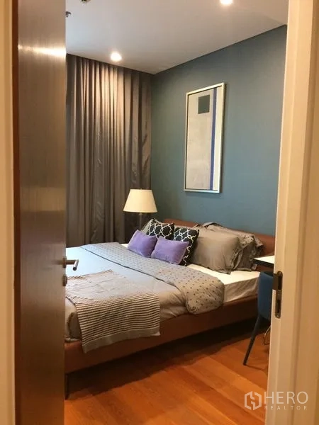 Condominium for rent in Khlong Toei, Bangkok - Bedroom with blue accent wall, upholstered bed, layered cushions, and blackout curtains.