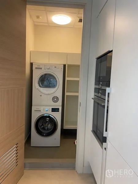 Condominium for rent in Pathum Wan, Bangkok - Utility room with stacked washer and dryer plus storage shelves and built-in ovens.