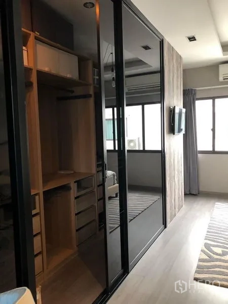 Townhouse for rent in Lat Phrao, Bangkok - Built-in walk-in closet with wood shelving and glossy black sliding wardrobe doors.